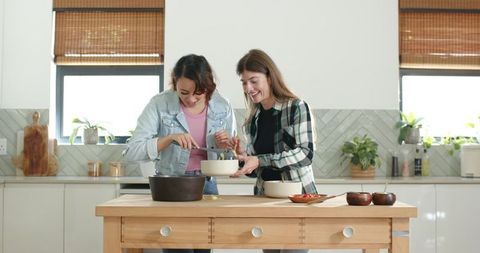 Two friends cooking and laughing in bright modern kitchen with wooden island
