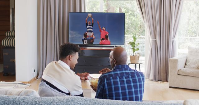 Father and son watching rugby match together in living room, bonding over favorite sport. Scene capturing family time, sports enthusiasm, and domestic comfort. Perfect for content focusing on family relationships, home entertainment, sports fandom, and modern living.