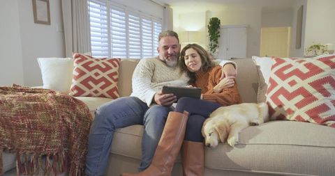 Couple Relaxing on Sofa with Sleeping Dog, Browsing Tablet at Home