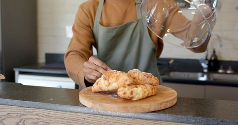African American barista placing glass cloche over fresh croissants on board cafe counter