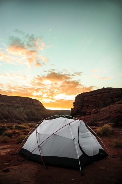 Isolated tent set up in rugged desert landscape with beautiful orange sunset sky. The scene conveys the adventure and serenity of outdoor camping and can be used to promote outdoor gear, travel destinations, wilderness adventures, and nature retreats.