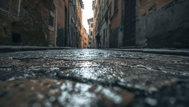 Shimmering wet cobblestone alley leading through historic narrow street to distant light