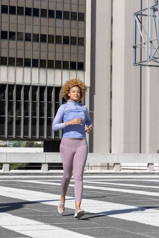 African american woman jogging in sunlit urban plaza wearing pastel activewear and wrist tracker