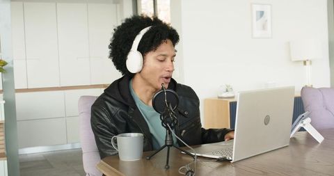 African american man recording podcast at home with headphones, microphone and laptop