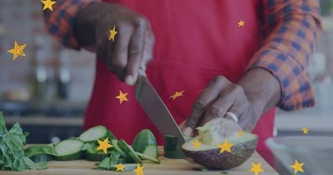 Home cook slicing avocado and cucumber on wooden board in red apron and plaid shirt