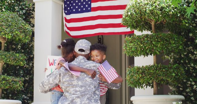 Soldier in military uniform hugging children under American flag. Ideal for themes of patriotism, military homecoming, family reunification, and national holidays like Independence Day. Suitable for use in articles about military service, support for troops, and family emotional reunions. Great for greeting cards, social media posts, and advertisements focused on family and national pride.