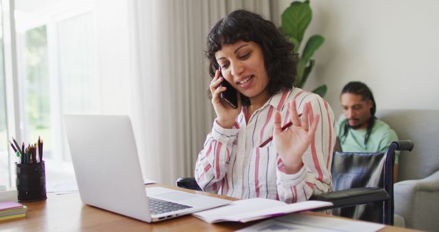 Woman in striped shirt working from home using phone and laptop - Download Free Stock Images Pikwizard.com