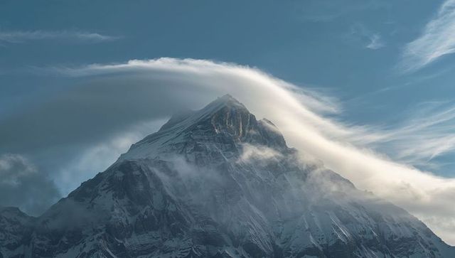 Lenticular cloud draping snow-capped alpine peak, windswept mist clinging slopes