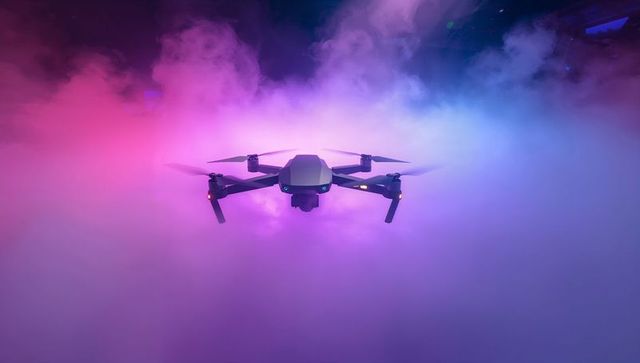 Hovering quadcopter drone amid magenta cyan fog with foldable arms and gimbal