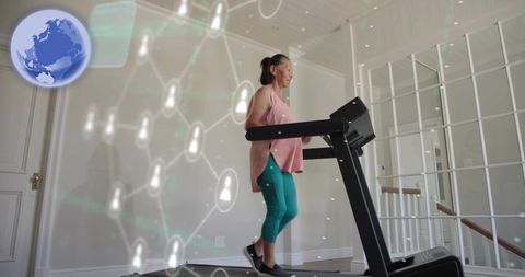 Senior asian woman walking on treadmill at home with digital health network overlay