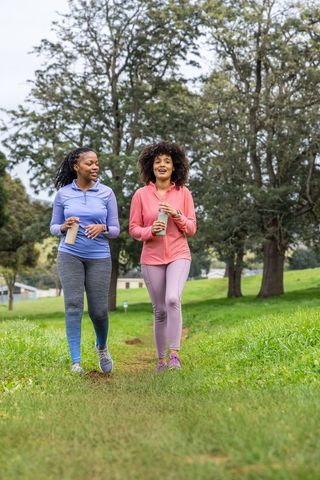 African american women walking in park holding reusable bottles, outdoor fitness duo