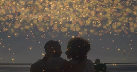 Silhouetted couple embracing on pier at twilight with golden bokeh lights