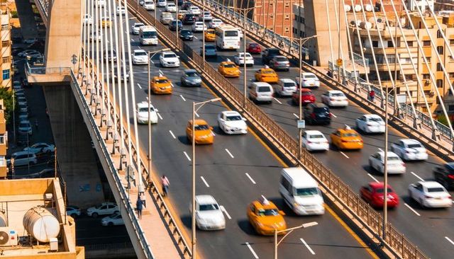 Busy cable-stayed bridge traffic with yellow taxis, pedestrians on elevated urban highway