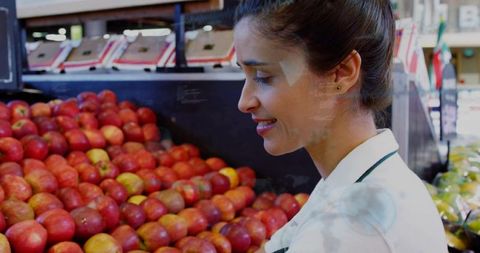 Grocery clerk restocking red apples on produce display smiling retail worker in uniform