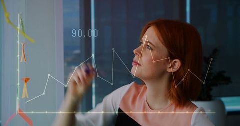Red-haired professional marking data point 90.00 on glass board in modern office