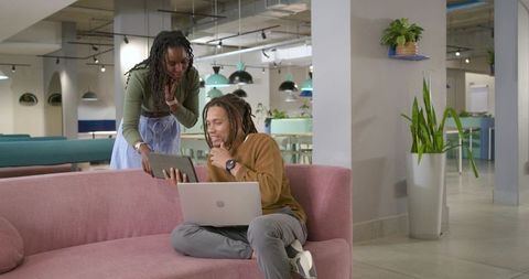 African american coworkers collaborating on laptop and tablet in pastel coworking lounge