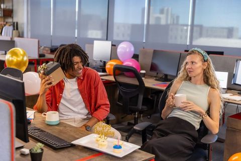 Cheerful Coworkers Celebrating Birthday with Gifts and Cupcakes in Office