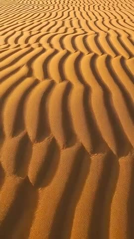 Vertical video moving over desert dunes revealing sand ripples and long shadows