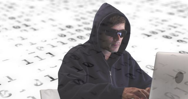 Hooded person wearing sunglasses typing on a laptop against a background filled with binary code. Useful for illustrating concepts related to cyber security, hacking, data protection, cyberspace, or cyber crime.