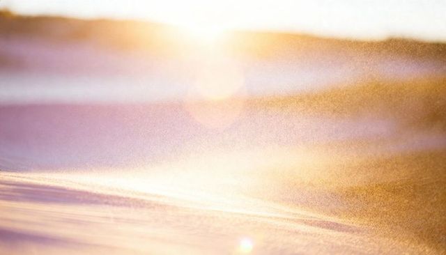 Golden morning sand blowing across beach at sunrise with lens flare glow