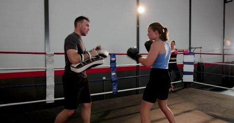Female Boxer Training with Coach Hitting Focus Pads in Boxing Ring Under Studio Lights