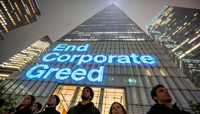 Skyscraper projection 'end corporate greed' illuminating nighttime urban protest crowd