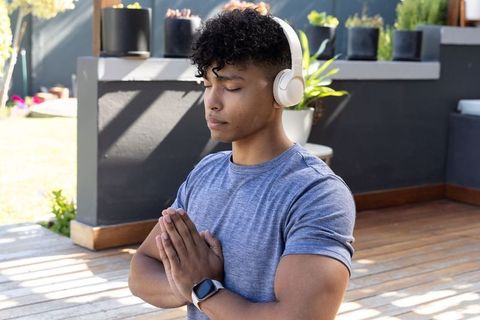 Young male meditating on sunlit wooden deck wearing headphones and smartwatch