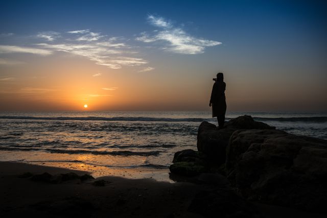 Woman Standing on Rocks Watching Sunset Over Shoreline - Download Free Stock Photos Pikwizard.com