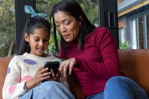 Asian mother and daughter sharing smartphone moment on cozy living room couch, bonding
