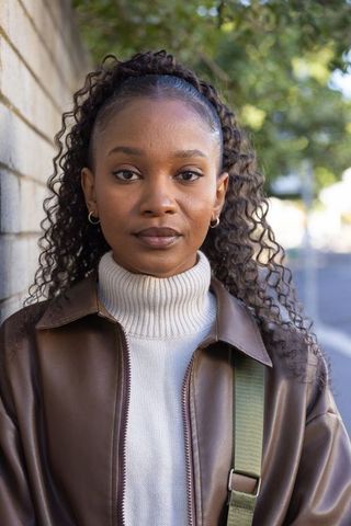 African american woman standing on urban sidewalk wearing brown leather jacket