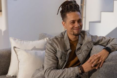 Smiling african american man relaxing on gray sofa in minimalist modern living room
