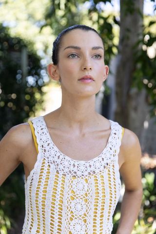 Sunlit garden portrait of woman wearing white crocheted top over yellow tank, looking upward