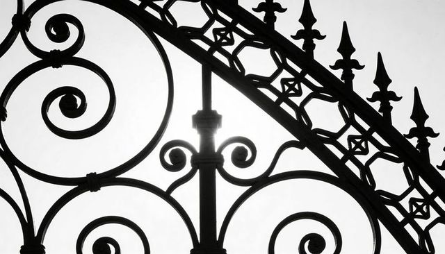 Ornate wrought-iron gate silhouetting sunlit scrollwork, spirals and spiked finials