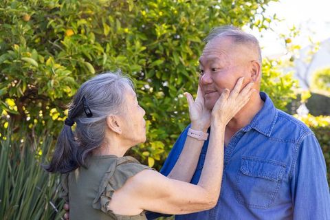 Asian senior couple sharing tender moment in sunny garden woman cupping partner's face