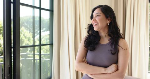 Smiling woman standing by sunlit black-framed sliding door looking out, relaxed home scene