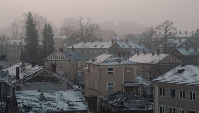 Foggy winter rooftops in quiet town with snow-dusted chimneys and muted pastel dawn tones