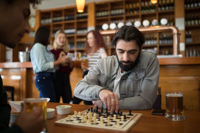 Men enjoying a game of chess while drinking beer in a bar. Ideal for concepts related to leisure activities, socializing, strategy games, and casual gatherings. Suitable for use in articles, advertisements, and promotions for bars, pubs, and social events.