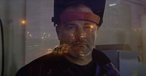 Welder at Workshop at Night with City Reflections