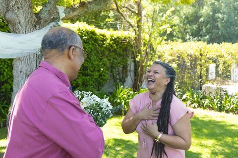 Joyful senior couple sharing surprise bouquet in sunlit backyard