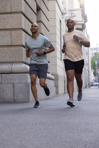 African american men running together on urban sidewalk with fitness watches and activewear