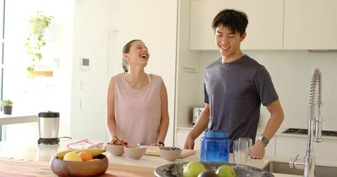 Young couple preparing breakfast in bright modern kitchen laughing while arranging fruit