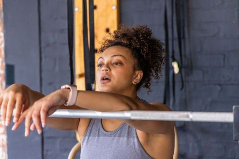 African American woman leaning on barbell after strength workout wearing smartwatch