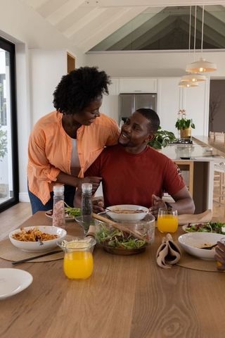 African american couple sharing cozy meal at wooden dining table in modern sunlit kitchen