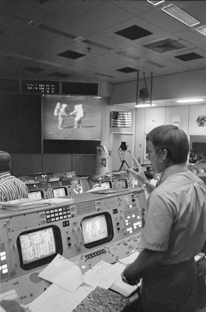 Flight director Gerald D. Griffin is overseeing Apollo 15's third EVA from Mission Operations Control Room. Astronauts David R. Scott and James B. Irwin are visible on the screen, collecting samples on the Moon's surface. Useful for history of space exploration, NASA missions, and team control operations.