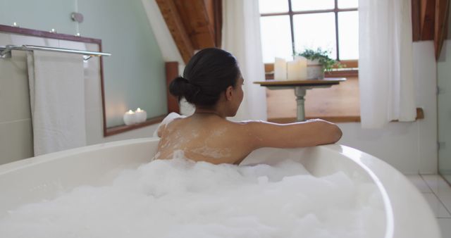 Woman enjoying a peaceful bubble bath in a calm bathroom environment with soft lighting and lit candles. Perfect for use in wellness and self-care ads, home decor blogs, spa and relaxation promotions, and articles focused on personal health and well-being.
