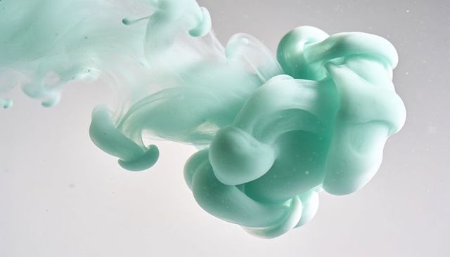 Billowing mint pigment swirling and diffusing in clear fluid with microbubbles