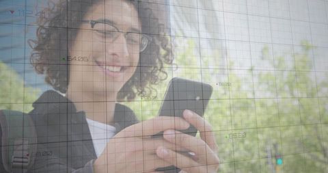 Smiling young man using smartphone with digital grid overlay on campus greenery