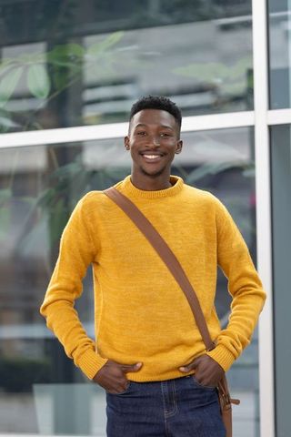 African american man standing smiling in mustard sweater carrying brown crossbody bag