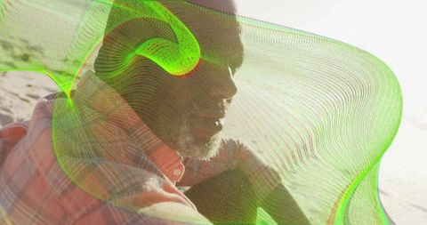 Mature man sitting on sunlit beach wearing plaid shirt and neon mesh overlay