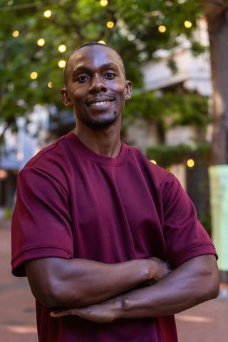 Confident african american man smiling with folded arms under string lights at twilight